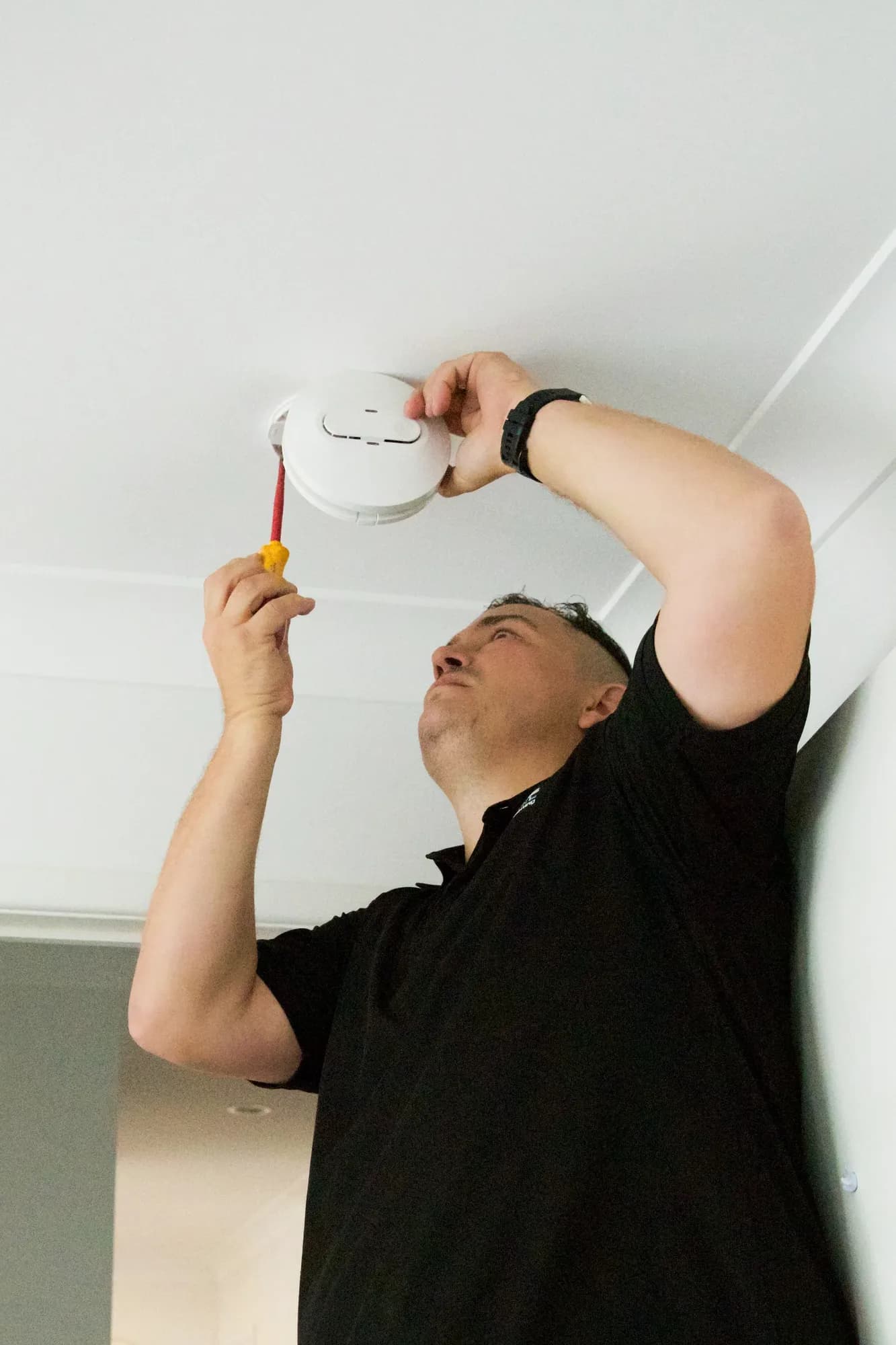 Spanos ElectriCool technician upgrading a ceiling smoke alarm in Brisbane